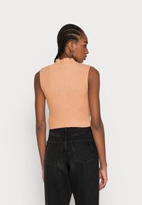 Top canalizado, sem mangas, na cor pêssego claro, com um pescoço alto e tecido texturizado. Combinado com jeans pretos de cintura alta.