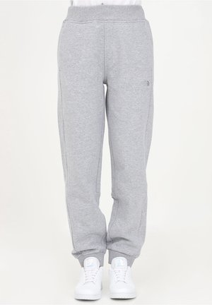 Pantalon de survêtement gris clair avec taille et poignets élastiques, porté avec des baskets blanches, vue de face sur un fond neutre.