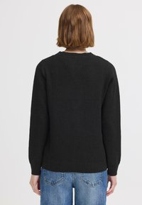 Pull en tricot noir à manches longues, col rond et ourlet côtelé. Porté avec un jean en denim bleu clair, montrant une coupe décontractée.