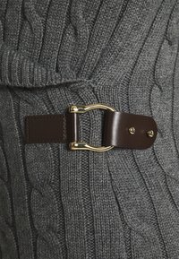 Detailní záběr na tmavě šedou pletenou tkaninu s hnědým koženým popruhem se zlatou kovovou sponou a dvěma zlatými nýty.