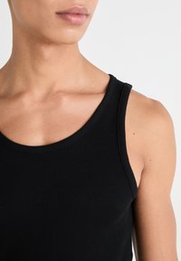 Débardeur noir à côtes avec un col rond, présentant des bretelles larges et une silhouette ajustée. Texture de tissu lisse et extensible.