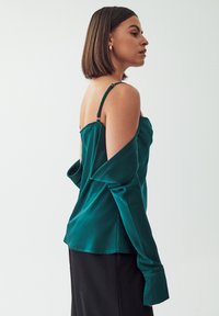 Turkusowa bluzka satynowa z cienkimi ramiączkami, fasonem off-shoulder, długimi rękawami i gładką teksturą. Posiada subtelny połysk i luźny krój.
