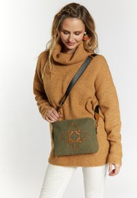 Grøn læder crossbody taske med et dekorativt brunt broderet mønster, en lynlåslukning og en justerbar rem. Tekstureret, glat overflade.