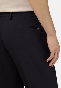 Tmavě námořnické kalhoty s elegantním designem, hladkým povrchem a zadní kapsou na zip s jemným metalickým akcentem.