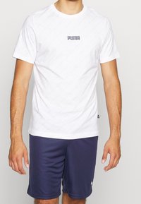 Bílý tričko s krátkým rukávem a texturovaným vzorem s šedým logem Puma na hrudi, kombinované s námořnickými šortkami s bílým logem.