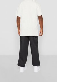 Světle šedé tričko s krátkým rukávem v kombinaci s černými cargo kalhotami se bočními kapsami, obuté s bílými teniskami. Jednoduchý, volnější střih.