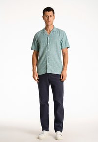 Korte mouwen, mintgroene, button-up shirt in een gestructureerde stof, gecombineerd met marineblauwe broek en witte sneakers.