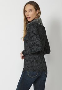 Schwarzes Langarmshirt mit einem strukturierten Blättermuster und einem grauen, gestrickten Kragen. Kombiniert mit dunkelblauen Jeans.
