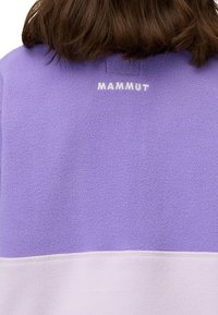 Pullover in pile viola con un logo bianco sul retro. Il design presenta uno stile a blocchi di colore con una sezione inferiore di un viola chiaro.