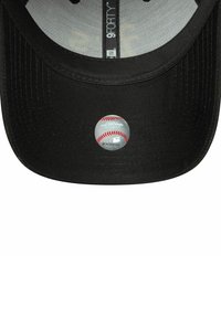 Gorra negra con visera plana. Presenta una etiqueta circular que representa un béisbol, con costura roja y texto gris. En el interior muestra un forro de marca.