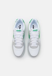 Bílé atletické boty s šedými a zelenými akcenty, s hladkým povrchem, zaoblenou špičkou a šněrovacím designem. Branding viditelný na jazyku.