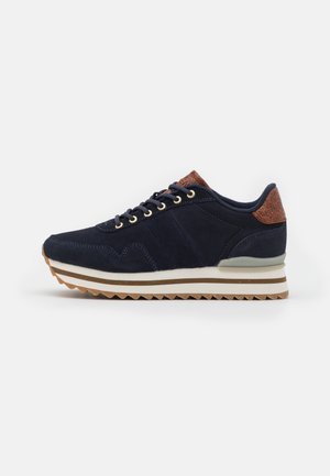 Navy suede sneaker with gold eyelets, a brown leather accent at the heel, and a white zigzag sole. Features a contrasting white midsole.