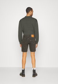 Calções de ganga cinza escuro com uma cintura ajustada e bolsos traseiros, usados com uma camisa de manga longa verde escura e botins pretos.