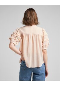Blusa rosa chiaro con maniche corte arricciate, vestibilità comoda e sottili righe verticali. Tessuto morbido e testurizzato con dettagli di bottoni.