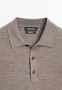 Braunes Merinowoll-Poloshirt mit klassischem Kragen, ausgestattet mit zwei schwarzen Knöpfen und einem strukturierten Strickmuster. Etiketten sind innen am Kragen sichtbar.