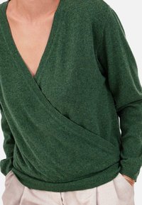 Grüner Strickpullover mit tiefem V-Ausschnitt und Wickeldesign. Verfügt über gerippte Bündchen und Saum. Weiche Textur, geeignet zum Schichten.