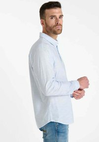 Lichtblauwe, lange mouwen shirt met verticale witte strepen, button-down kraag en een ontspannen pasvorm. Gedragen met blauwe jeans, wat een casual stijl uitstraalt.