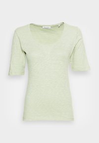 T-shirt aderente verde chiaro con maniche corte, caratterizzato da un colletto a girocollo. Realizzato in tessuto testurizzato, leggermente trasparente, con un motivo sottile.