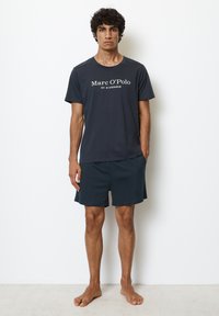Marineblå T-shirt med hvidt logotekst, parret med matchende mørke shorts. Casual stil, korte ærmer og en afslappet pasform.