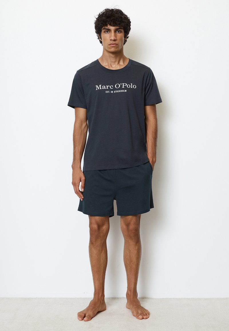 Marineblå T-shirt med hvidt logotekst, parret med matchende mørke shorts. Casual stil, korte ærmer og en afslappet pasform.