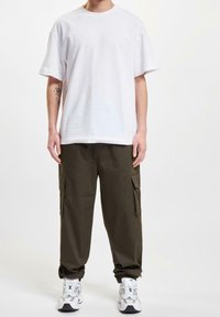 Wit katoenen T-shirt met een ontspannen pasvorm, gecombineerd met olijfgroene cargobroeken met meerdere zakken. Witte sneakers maken de outfit compleet.