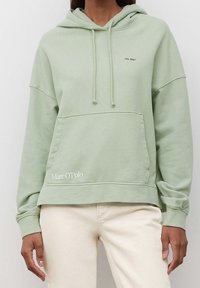 Sudadera verde claro hecha de tela suave, con un bolsillo frontal, capucha con cordón y el logo "Marc O'Polo" impreso en el dobladillo.
