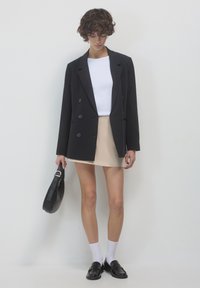 Blazer nero doppiopetto, t-shirt bianca, mini gonna beige, mocassini neri e calzini bianchi, con una borsa nera. Design semplice e vestibilità sartoriale.