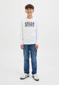 T-shirt bianca a maniche lunghe con grafica "JACK & JONES" multicolore. Abbinata a jeans blu e sneakers grigio-neri con dettagli bianchi.