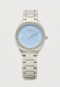 Sølvfarvet Guess-ur med lyseblå urskive, pyntet med krystaller og en tekstureret baggrund. Har et armbånd i rustfrit stål.