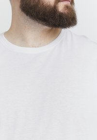 Weißes Baumwoll-T-Shirt mit rundem Halsausschnitt, strukturiertem Stoff und einem klaren, minimalistischen Design. Fokus auf dem Halsausschnitt und Schulterbereich.