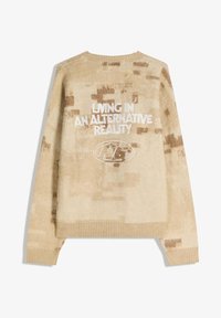 Beige tröja med mjuk textur, med ett pixlat mönster, rund halsringning och broderad text "LIVING IN AN ALTERNATIVE REALITY."