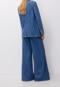 Denim blazer and wide-leg pants in medium blue. The blazer features a vent and buttoned cuffs; pants have a loose fit with a straight leg.