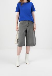 Niebieska koszulka z krótkim rękawem, szare dżinsowe culottes, białe botki za kostkę i beżowa torebka. Prosty design bez widocznych wzorów czy akcentów.