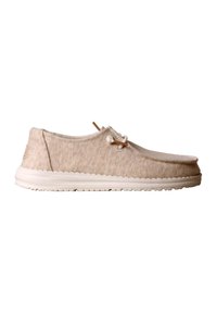 Chaussure décontractée beige à enfiler avec semelle blanche, coutures style mocassin, et détail décoratif en lacet de cuir sur le côté.