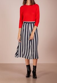 Czerwony sweter z dzianiny o trzech czwartych rękawach w połączeniu z granatową i białą spódnicą midi w paski. Modelka nosi czarne botki za kostkę.
