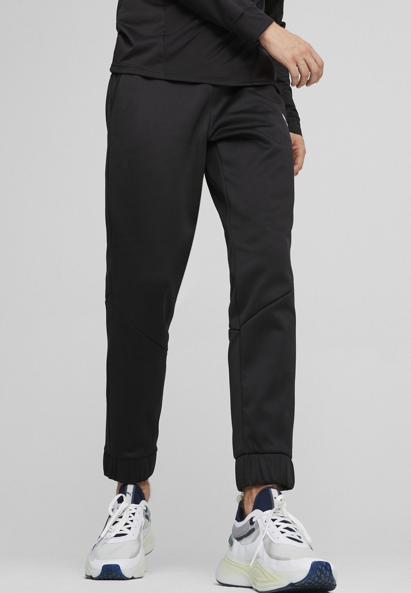 Sorte atletiske bukser lavet af glat stof har en tapered design, elastiske manchetter og søm detaljer. Båret med hvide og marineblå sneakers.