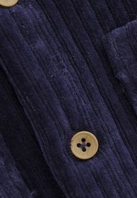 Tissu en velours côtelé bleu marine avec une texture côtelée, orné d'un bouton en bois au centre, présentant quatre trous et une finition lisse.