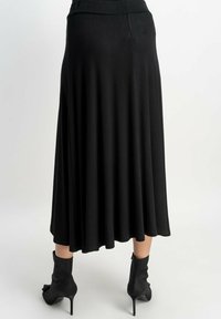 Czarna, sięgająca do kolan spódnica w kształcie litery A, wykonana z gładkiego materiału o lekko błyszczącej powierzchni. Połączona z czarnymi botkami na obcasie.