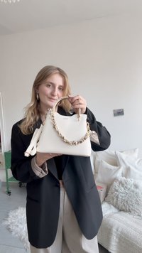 Sac à main blanc de forme structurée, avec une anse en chaîne dorée et une surface texturée lisse. Une bandoulière amovible est incluse.