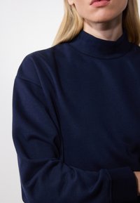 Sudadera de cuello alto en azul marino con una textura suave y un corte holgado. Presenta hombros caídos y mangas largas. Sin patrones ni acentos visibles.