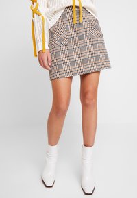 Falda corta de cuadros en tonos naranja y negro, con bolsillos frontales y un diseño ajustado. Combinada con botines blancos.