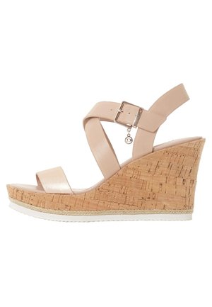 Beige kileformet sandal med korkplatform, ankelrem med spænde og en lille rund vedhæng, der hænger fra spændet.