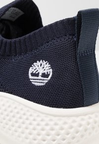 Baskets en maille bleu marine avec une tige texturée, une semelle en caoutchouc blanche et un logo brodé. Accents lisses et col élastique pour un enfilage facile.