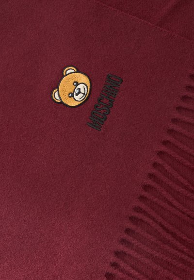 Écharpe bordeaux aux bords effilochés, brodée d'un petit visage d'ourson et du mot "MOSCHINO" en fil noir.