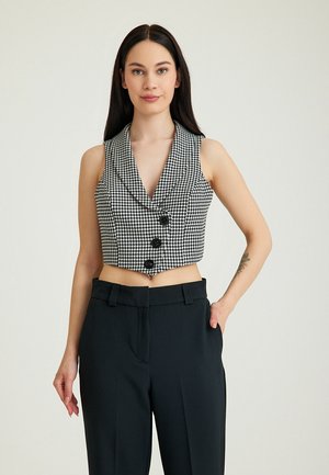 Geknipte, mouwloze zwart-wit houndstooth vest met een diepe V-hals en drie grote knopen. Gepaard met hoge taille zwarte broek.