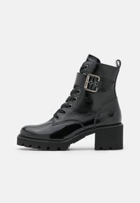Bottines noires à finition brillante, avec un laçage sur le devant, un accent de boucle, un talon épais et une semelle texturée.