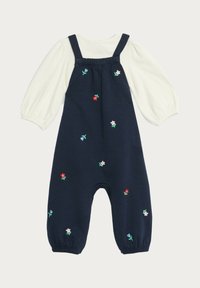 Marinblå overall med broderade blommönster, med en vit långärmad topp under och resår i benöppningarna.