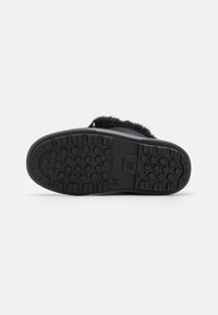 Calzado negro con una suela de goma texturizada que presenta empuñaduras redondeadas para mayor tracción. Los acentos de piel suave en la parte superior realzan el diseño.