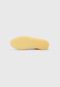 Rubber shoe sole in yellow, features a textured surface with patterns for grip, rounded shape, and a smooth edge.