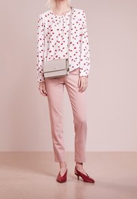 Blusa bianca con motivo floreale rosso, pantaloni rosa chiaro, tacchi rossi e una borsa a tracolla grigia con dettagli dorati e tracolla a catena.
